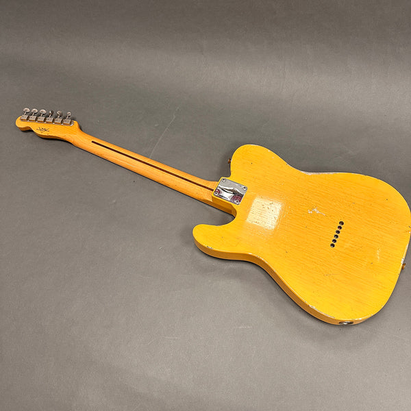 Back view of vintage yellow electric guitar with worn finish and bolt-on neck on gray background