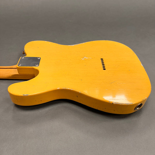 Close-up of the back body of a vintage yellow solid-body electric guitar showing finish wear and aging cracks on a gray background