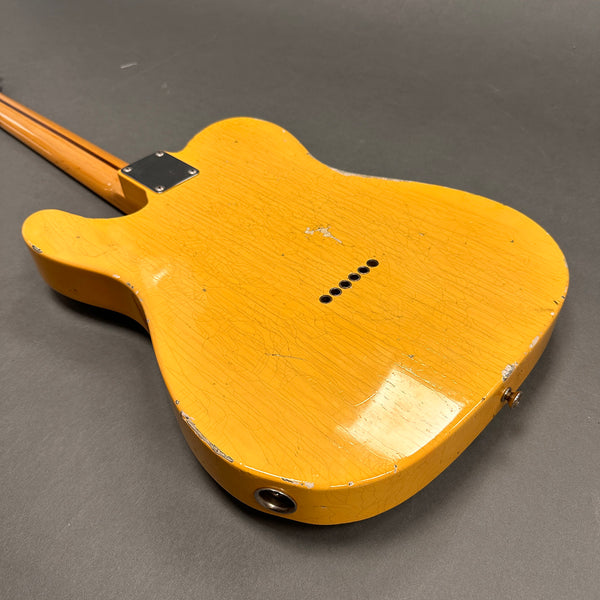 Back view of vintage yellow electric guitar body with visible wear and finish checking on gray surface
