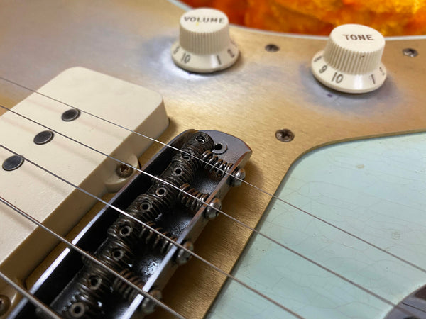 Close-up of vintage electric guitar bridge, volume and tone control knobs, cream pickup, and strings on a golden and light blue body finish