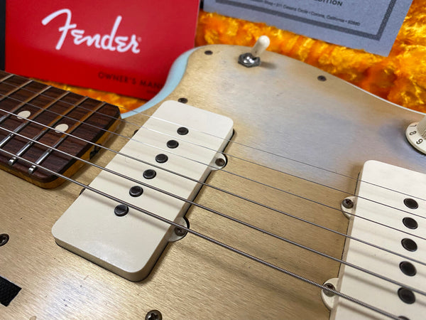 Close-up of vintage Fender electric guitar pickups and strings with partial view of rosewood fretboard and red Fender owner's manual in background