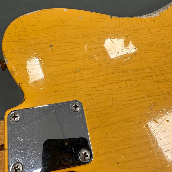 Close-up of vintage yellow electric guitar body with worn, cracked finish and metal neck plate screws visible