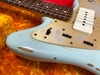 Close-up of light blue electric guitar body with gold pickguard, P90 pickup, and visible wear and paint chipping on orange plush background