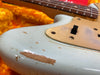 Close-up of vintage electric guitar body with light blue paint, showing wear and wood exposure near pickguard and switch, with rosewood fingerboard and strings.