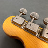 Close-up of vintage guitar tuning pegs on natural wood headstock with metal machine heads and flat tuning buttons against gray background