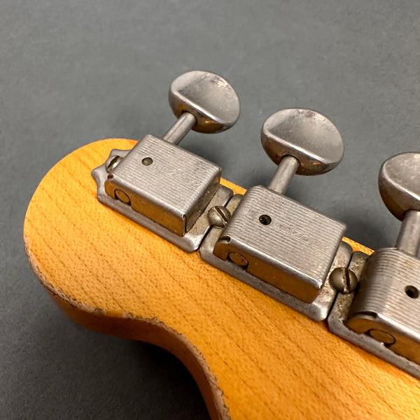 Close-up of vintage guitar tuning pegs on natural wood headstock with metal machine heads and flat tuning buttons against gray background