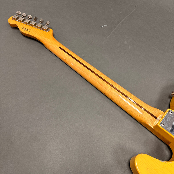 Back view of electric guitar neck with natural wood finish and vintage tuning pegs on gray background