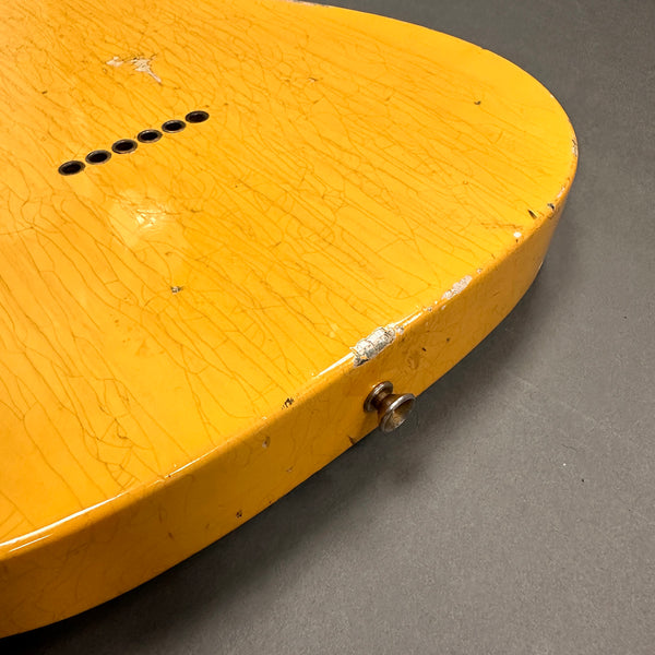 Close-up of the yellow aged and worn body of an electric guitar showing string ferrules and strap button on a gray background
