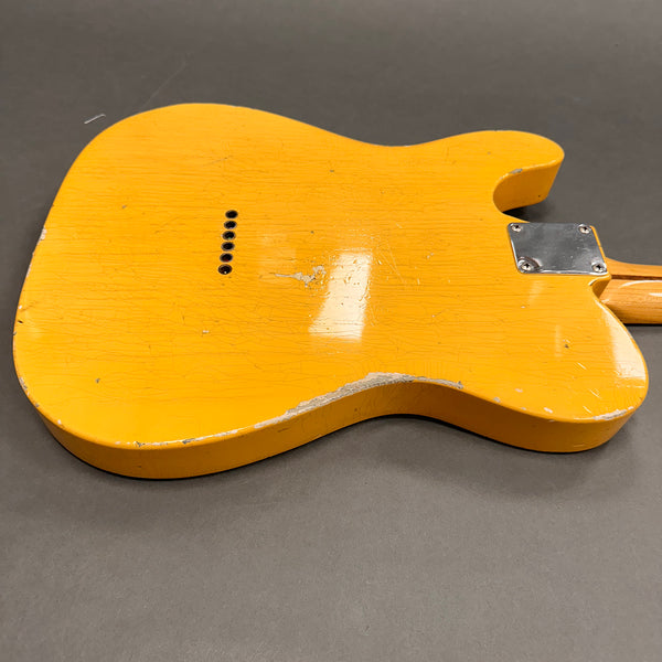 Close-up of the back of a vintage yellow electric guitar body with worn and chipped paint, showing string ferrules and metal neck plate on grey background