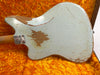 Back view of vintage electric guitar with worn white finish and visible wood, resting on plush orange guitar case lining