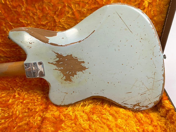 Back view of vintage electric guitar with worn white finish and visible wood, resting on plush orange guitar case lining