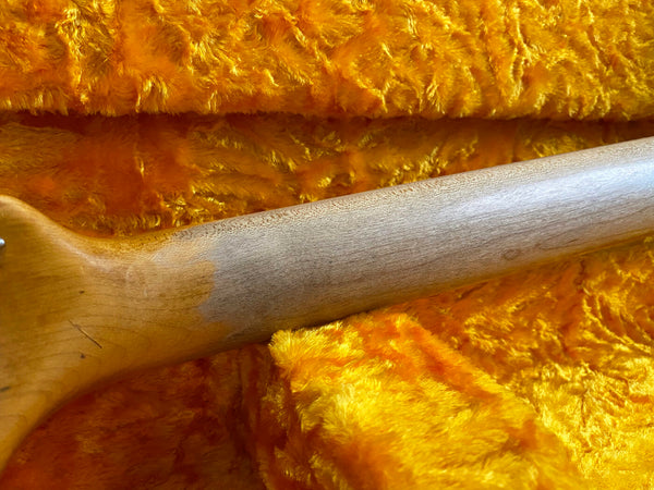Close-up of vintage guitar neck with worn wood finish resting on bright orange plush guitar case lining