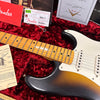 Close-up of vintage Fender Stratocaster electric guitar neck and body with sunburst finish, surrounded by Fender owner's manual, tremolo springs instructions, and Fender Custom Shop certificates on red velvet guitar case lining.