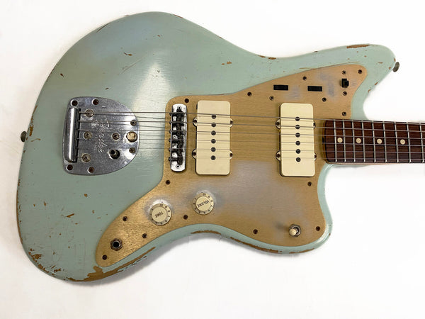 Close-up of vintage Fender Jazzmaster electric guitar body in seafoam green with gold pickguard, dual cream pickups, tone and volume knobs, and worn finish detailing