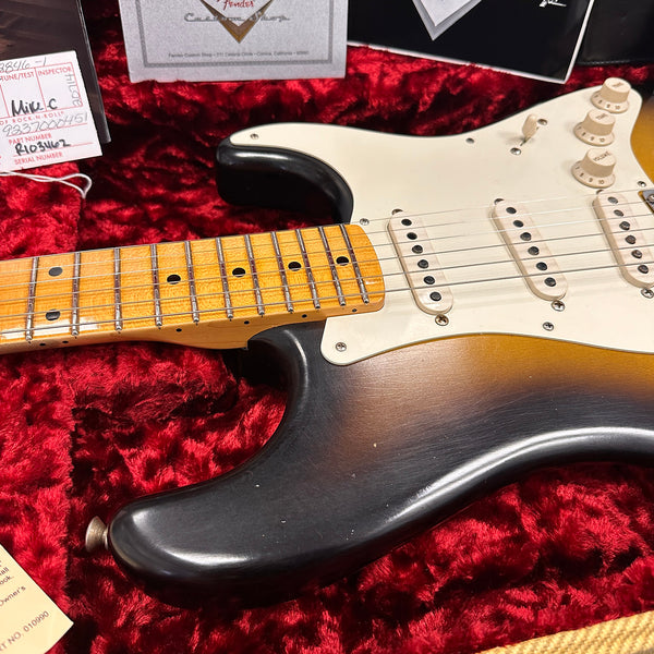 Close-up of sunburst Fender Stratocaster electric guitar body and maple neck with single-coil pickups, resting in red plush-lined case with Fender certificate and inspection tags.