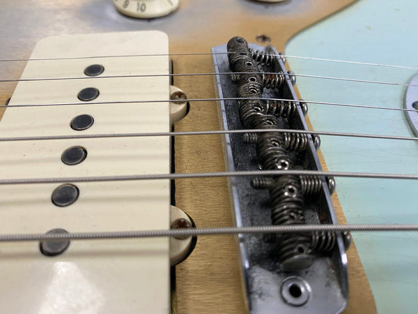 Close-up of vintage electric guitar bridge and single-coil pickup with string springs and aged hardware on natural wood finish body