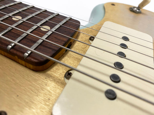 Close-up of electric guitar strings, pickups, and rosewood fretboard with dot inlays on a vintage-style guitar body