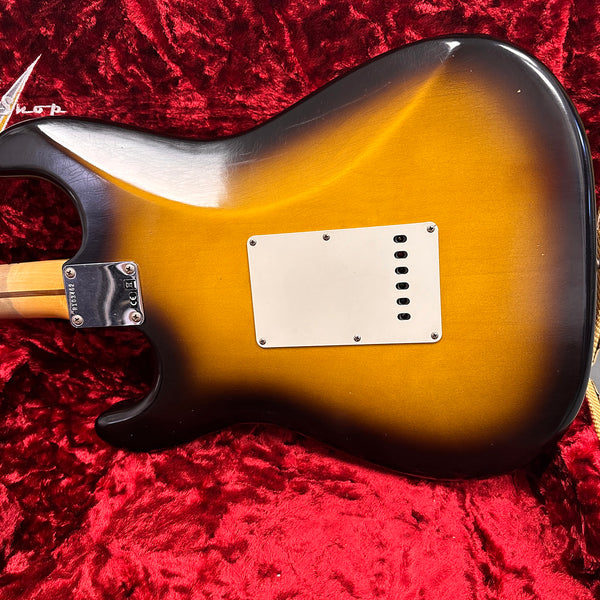 Back of sunburst finish electric guitar body with white tremolo cavity cover plate on red plush fabric background