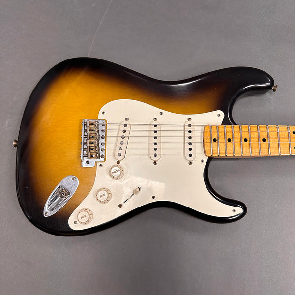 Sunburst electric guitar with maple neck, three single-coil pickups, white pickguard, and control knobs on gray background