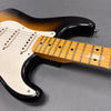 Close-up of sunburst electric guitar body and maple neck with white pickguard and single-coil pickups on gray background
