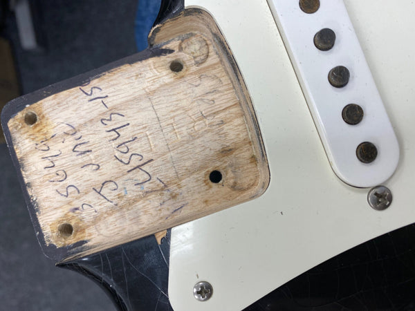 Close-up of vintage electric guitar neck pocket showing wood grain and handwritten markings, white single-coil pickup, black and cream guitar body with screws