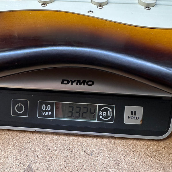 Electric guitar body showing sunburst finish on a DYMO digital scale displaying a weight of 3.324 pounds