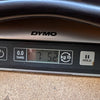 Close-up of Dymo digital scale display showing guitar weight of 7 pounds 5.2 ounces at Coffee House Guitars.