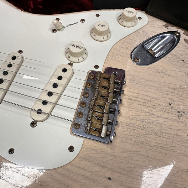 Close-up of vintage electric guitar bridge, volume and tone control knobs, and single-coil pickups on cracked cream-colored body