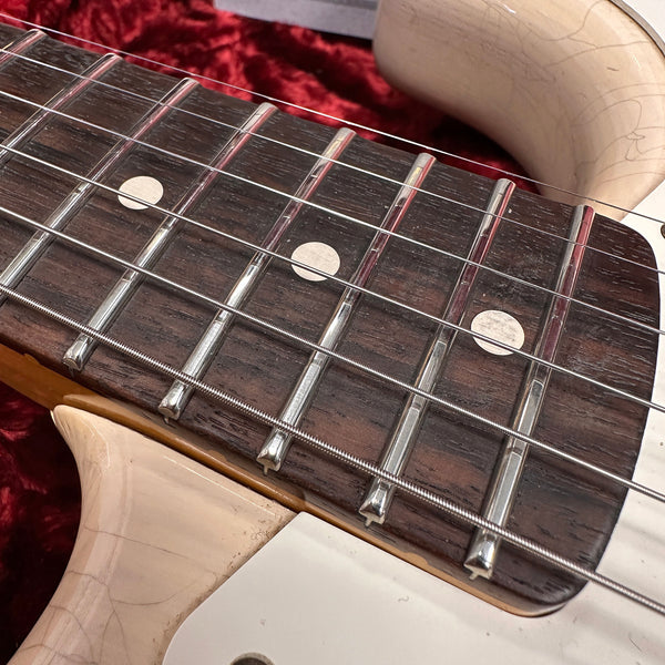 Close-up of electric guitar fretboard with white dot inlays, metal frets, and steel strings, showing wear and a cream-colored guitar body edge.