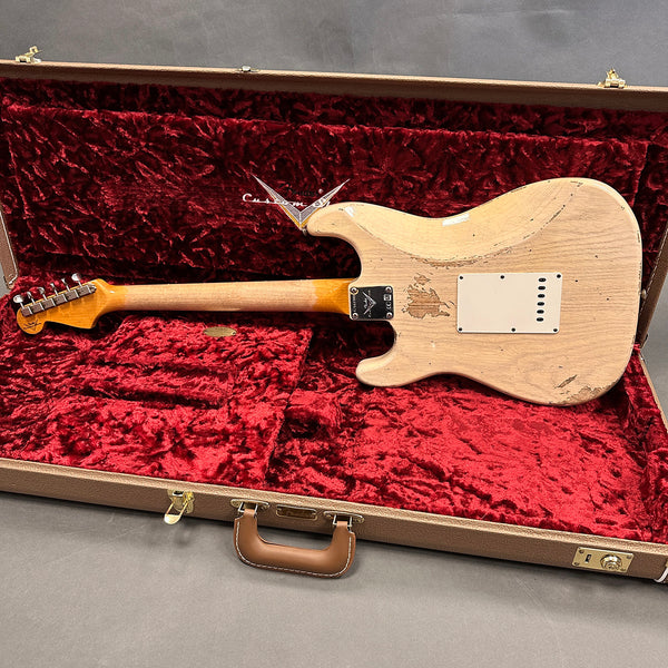 Back view of vintage Fender Stratocaster electric guitar with worn white finish inside a red velvet-lined brown hardshell guitar case