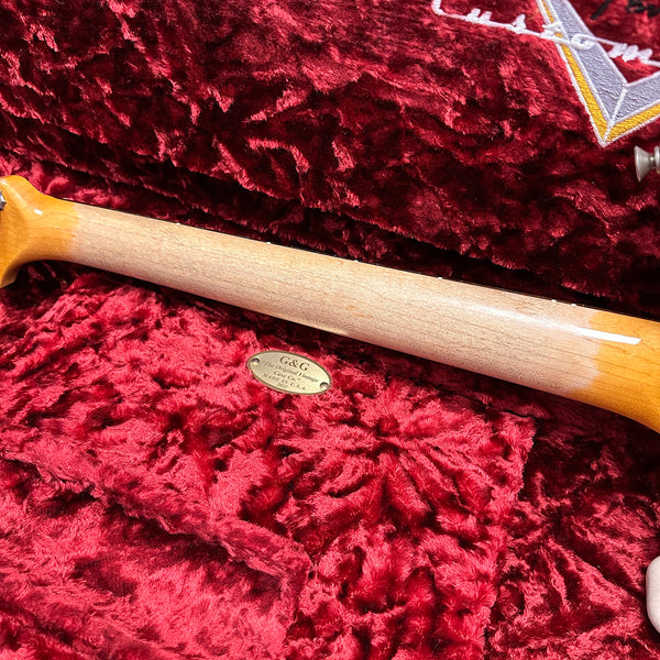 Close-up of guitar neck resting on plush red velvet lining inside a G&G The Original Vintage guitar case with gold emblem plate