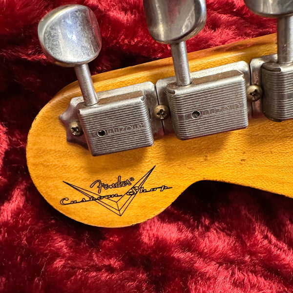 Close-up of Fender Custom Shop guitar headstock back showing tuning pegs and logo on wood against red plush background