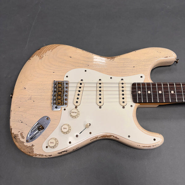 Close-up of vintage-style cream electric guitar body with three single-coil pickups, white pickguard, and worn finish showing wood grain and aging effects on gray background