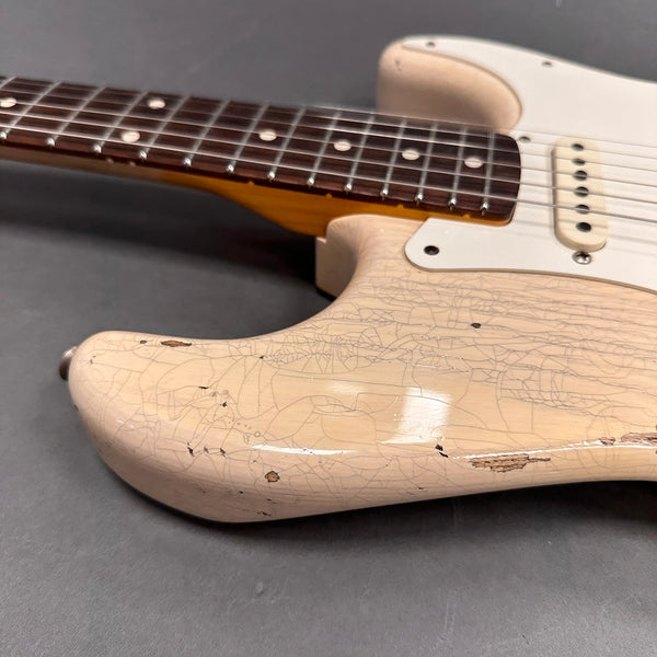 Close-up of vintage cream electric guitar body with worn and cracked finish, showing nitrocellulose lacquer aging and brown rosewood fretboard with dot inlays on gray background.