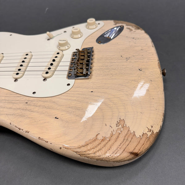 Close-up of vintage cream electric guitar body with worn finish and visible wood grain near bridge and control knobs on gray background