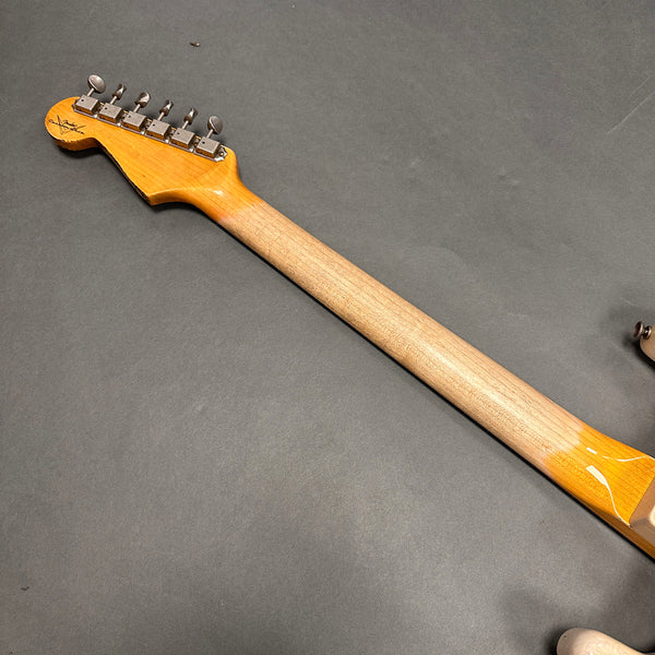 Back of a natural wood guitar neck with vintage-style tuning pegs on a dark background