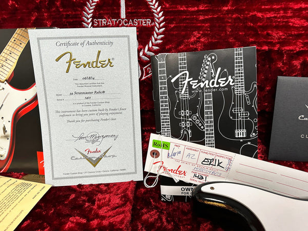 Fender Custom Shop Certificate of Authenticity for 54 Stratocaster Relic model dated 06/18/14, displayed with Fender warranty booklet, inspection tag and part of a black and white Fender guitar on red plush Stratocaster case lining.