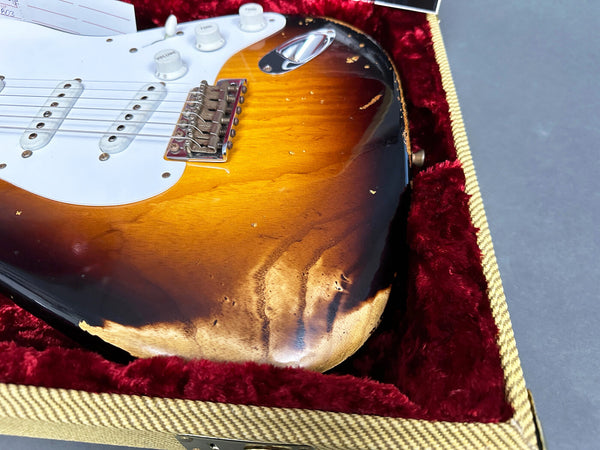 Close-up of a sunburst electric guitar body with visible wear and finish damage, resting inside a red plush-lined tweed guitar case