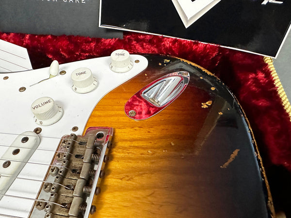 Close-up of sunburst electric guitar body showing volume and tone knobs, white pickguard, vintage bridge, and jack plate with visible wear and paint chips.