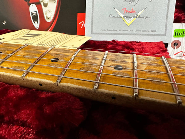 Close-up of vintage Fender electric guitar neck and frets with aged maple fretboard on red plush case lining with Fender Custom Shop certificate and documents in background