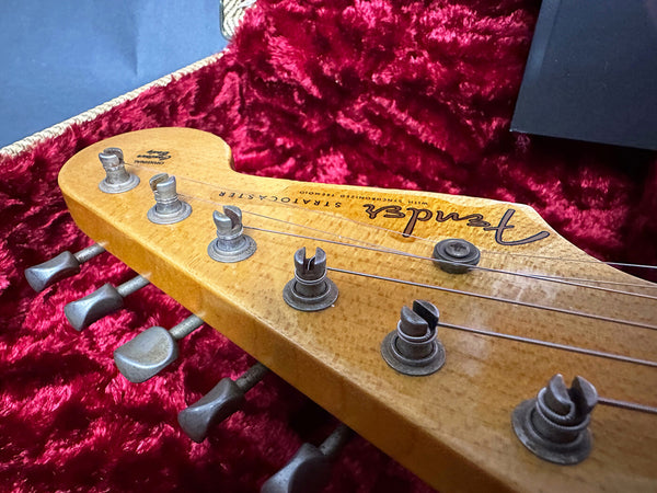 Close-up of vintage Fender Stratocaster guitar headstock with tuning pegs, in a red plush-lined guitar case