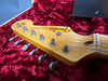 Close-up of vintage Fender Stratocaster guitar headstock with six tuning pegs on red plush interior guitar case lining