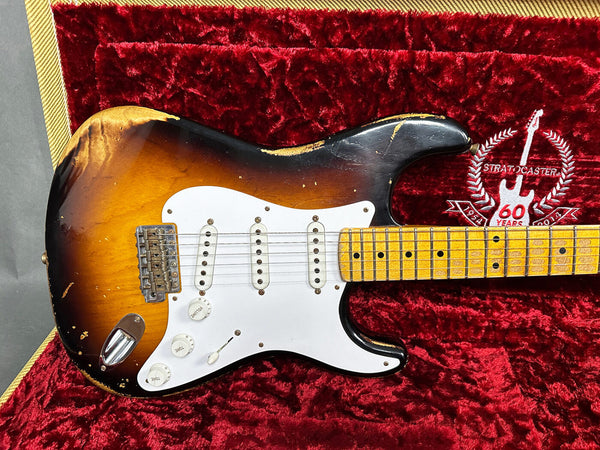 Vintage Fender Stratocaster electric guitar with sunburst finish and white pickguard, showing wear and aging, resting in red plush-lined hard case embroidered with "Stratocaster 60 Years 1954-2014" logo