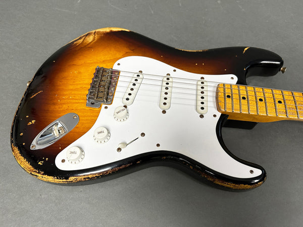 Vintage sunburst electric guitar with white pickguard and maple neck showing wear and relic finish on gray background