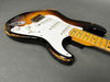 Vintage sunburst electric guitar with maple neck and white pickguard showing worn and chipped paint on body edges on gray background