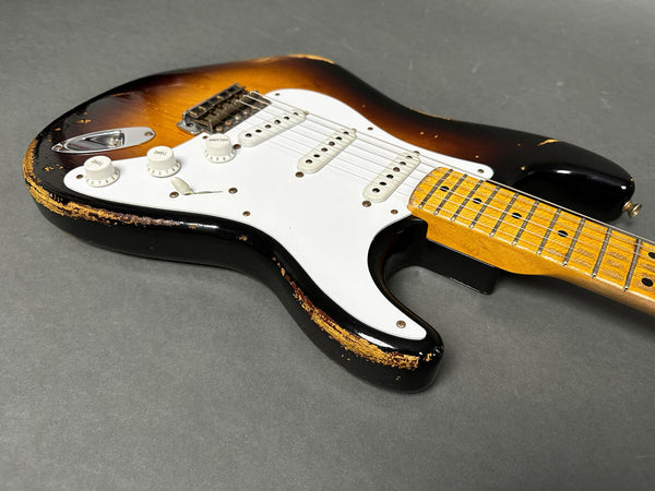 Vintage sunburst electric guitar with maple neck and white pickguard showing worn and chipped paint on body edges on gray background