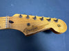 Close-up of vintage Fender Stratocaster guitar headstock with worn natural wood finish and tuning pegs against blue background