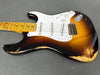 Vintage sunburst electric guitar with white pickguard and three single-coil pickups, showing worn and distressed finish on body and neck, lying on gray surface.