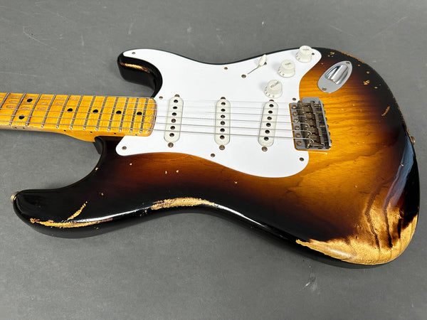 Vintage sunburst electric guitar with white pickguard and three single-coil pickups, showing worn and distressed finish on body and neck, lying on gray surface.
