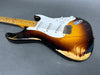 Vintage sunburst electric guitar with maple neck and white pickguard showing heavy wear and relic finish details on gray surface
